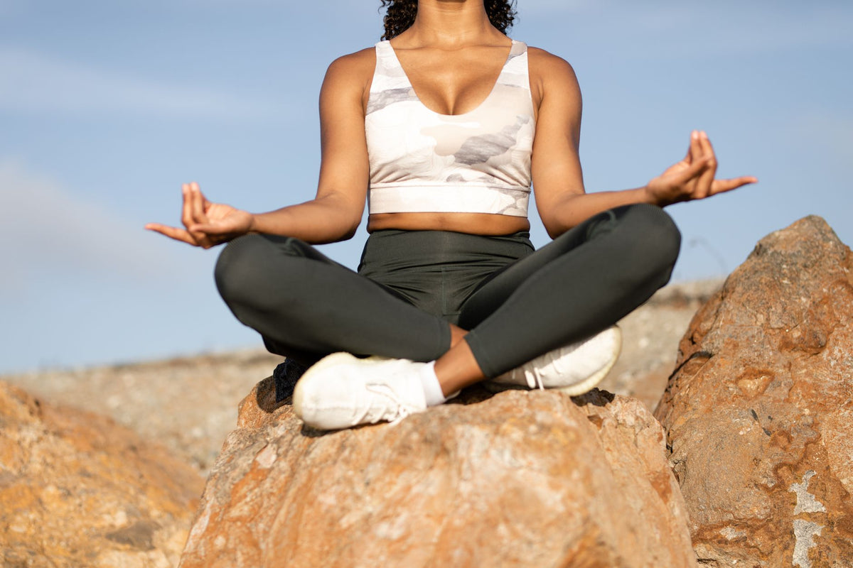 Woman meditating outdoors on rocks, promoting peace and mindfulness.