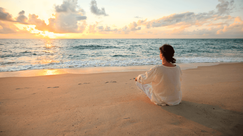 Woman meditating peacefully by the ocean at sunrise